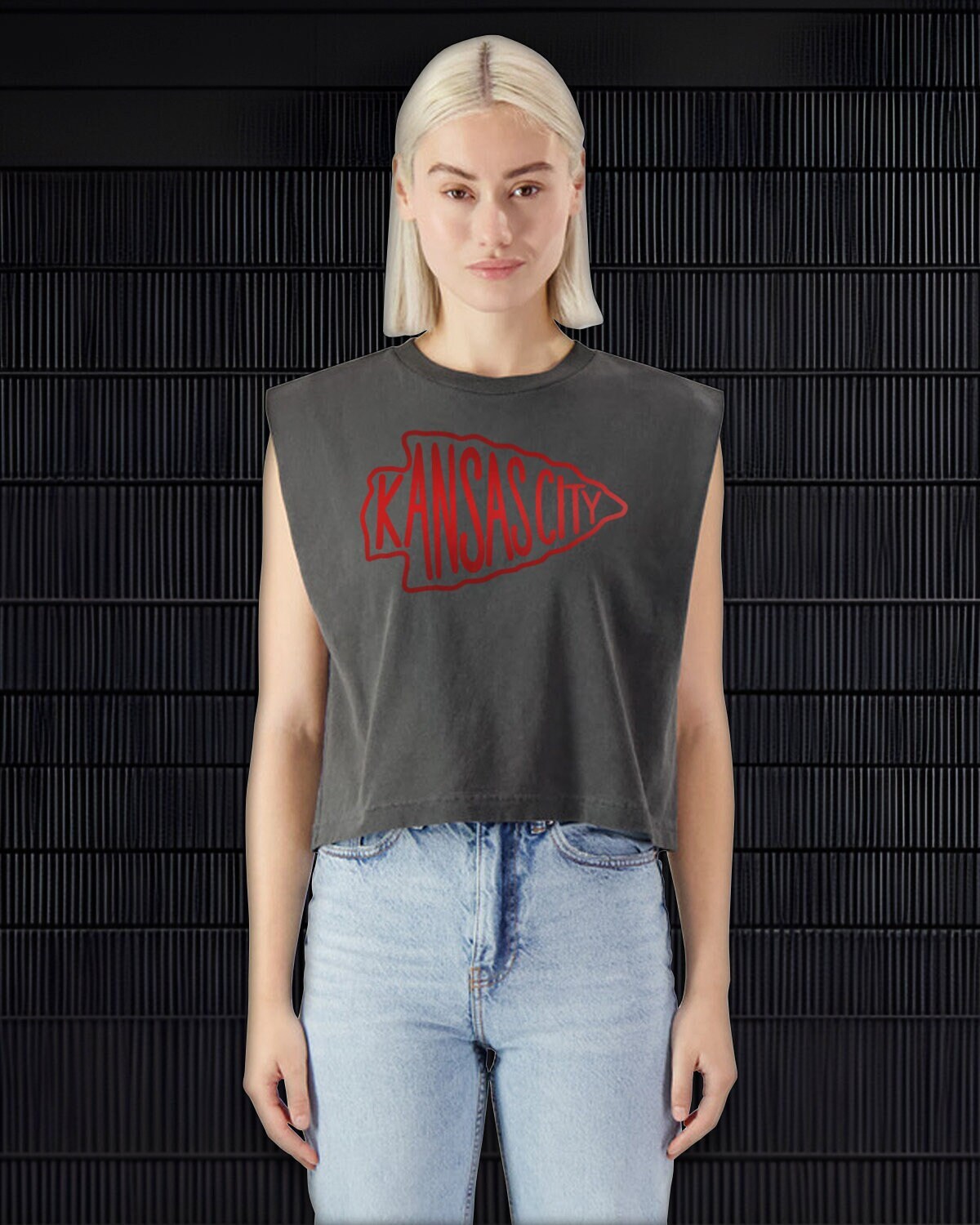 a woman wearing a dark grey cropped shirt with an arrowhead and jeans