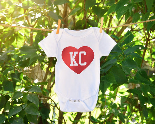 a white onesie with a red heart with KC cut out hanging on a clothes line