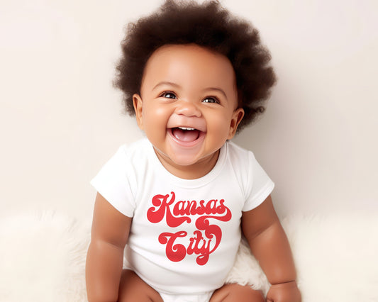 Baby wearing a white onesie with Kansas City in a retro font in red